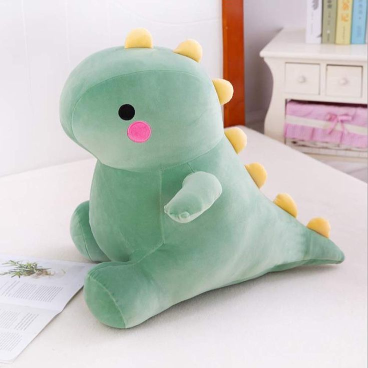 a green stuffed dinosaur sitting on top of a bed next to a piece of paper