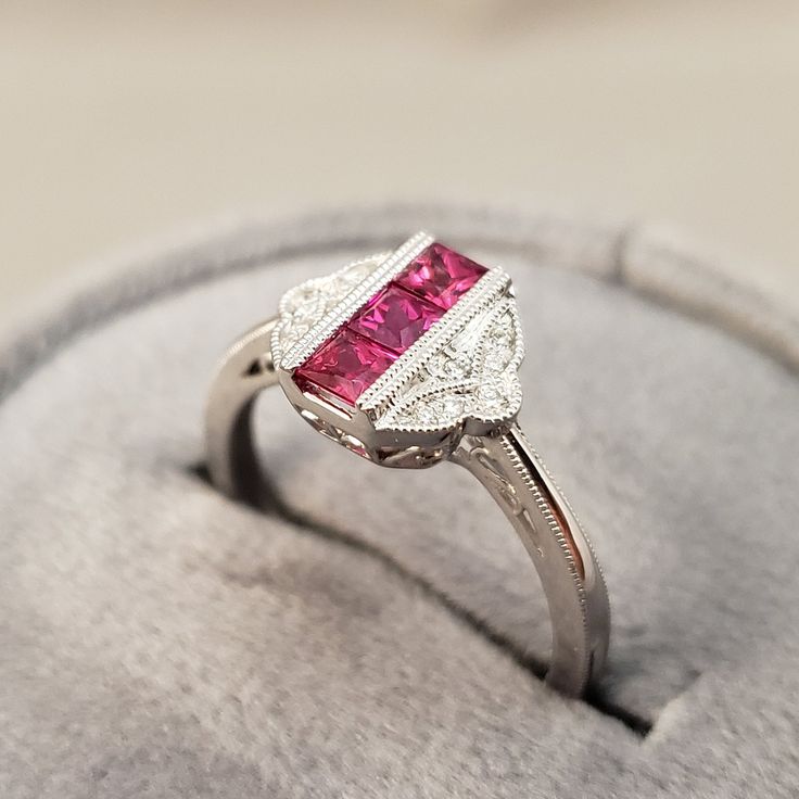 "July Birthstone! Bright Red Ruby Ring featuring 3 square Channel Set Genuine Ruby center stones (Ruby weight equalling .57ct) in a delicate vintage inspired filigree design full of Genuine White Diamonds, (Diamond weight equals .06 carats total) A Unique 14kt White Gold Ring, with Solid white gold bars known as a channel on the rubies & prongs on the diamonds add a bright finish while holding the stone firmly in place. This Ruby ring is perfect for everyday ware. **Ring size: 6.5 **Ruby is Fine Jewelry Ruby Ring With Center Stone For Anniversary, Fine Jewelry Ruby Ring With Center Stone For Promise, Exquisite 14k White Gold Promise Ring, Exquisite 14k White Gold Ring With Center Stone, Fine Jewelry Lab-created Ruby Promise Ring, Fine Jewelry Ruby Ring With Accent Stones For Promise, Ruby Rings With Diamond Cut In Round Band, White Gold Ruby Ring With Center Stone For Promise, Fine Jewelry Rings With Lab-created Ruby And Accent Stones