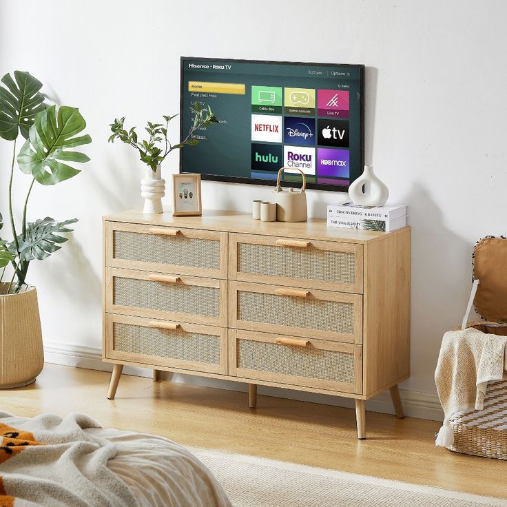 a flat screen tv sitting on top of a wooden dresser next to a potted plant