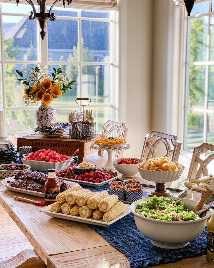 a table filled with lots of food on top of a wooden table next to windows