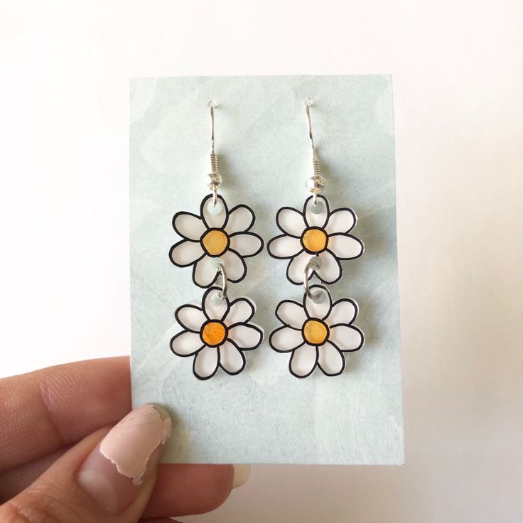 a pair of white and yellow flower earrings sitting on top of a piece of paper