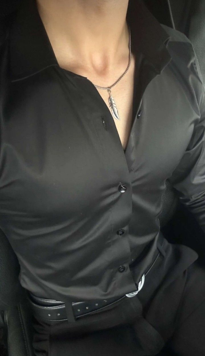 a man wearing a black shirt and tie in the back seat of a car with his hands on his hips