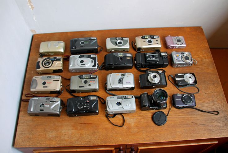 many different types of cameras sitting on a wooden table with wires attached to the top