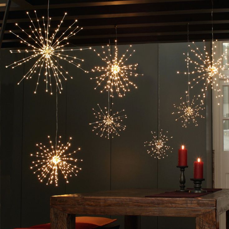 some lights are hanging from the ceiling above a dining room table with red chairs and candles