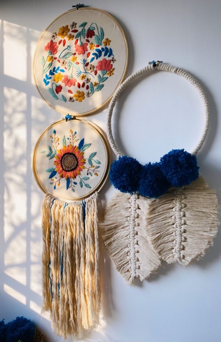 two handmade wall hangings with flowers and tassels on them, next to each other