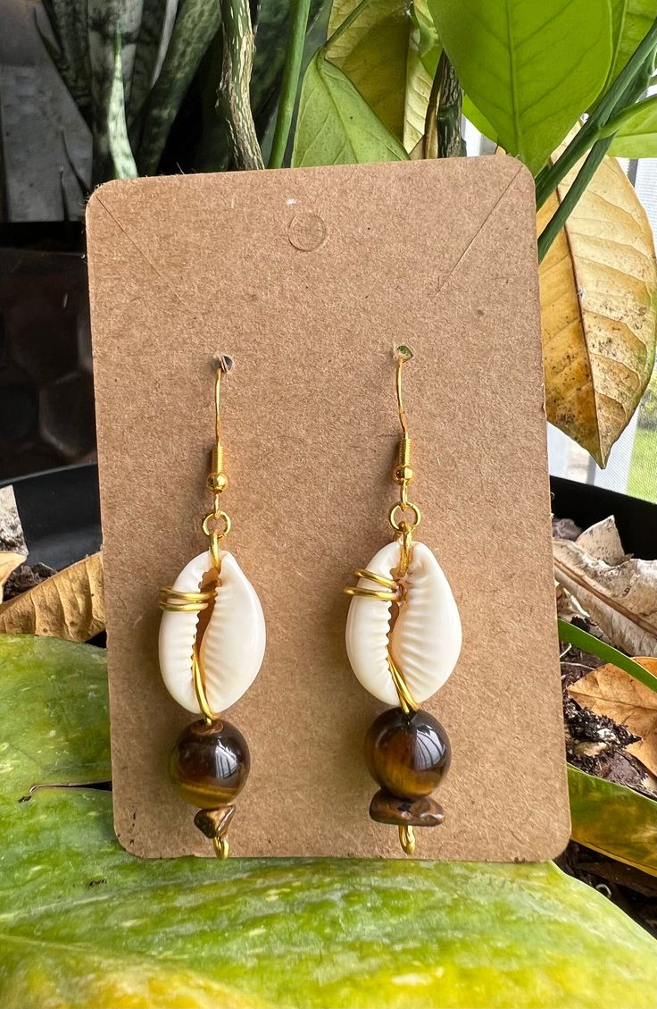 Natural Cowrie shell earrings! This beautiful piece will bring luck and protection to the wearer. Plus the Tigers eye to  add a touch of self confidence and inner strength.  Make a statement in this beautiful handmade wire wrapped piece.It dangles beautifully, for any, outings, occasions or a nice gift. Bohemian Wire Wrapped Jewelry For Vacation, Bohemian Shell Earrings For Jewelry Making, Handmade Dangle Jewelry For Vacation, Handmade Drop Earrings For Vacation, Hand Wrapped Brown Jewelry For The Beach, Brown Dangle Jewelry For Vacation, Handmade Shell Dangle Jewelry, Cowrie Shell Earrings, Cowrie Shell Jewelry Necklaces