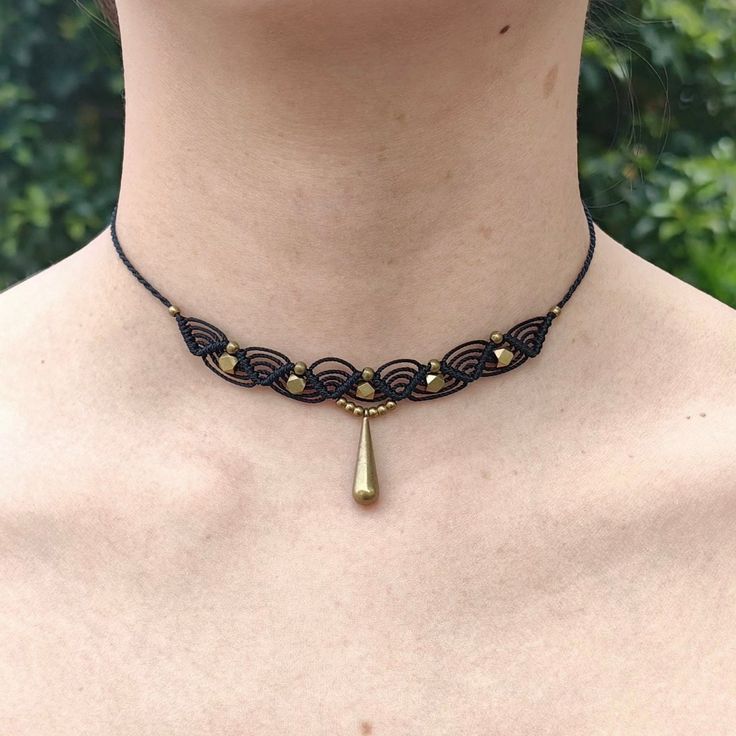 a woman wearing a black and gold choker with a tear shaped pendant on it