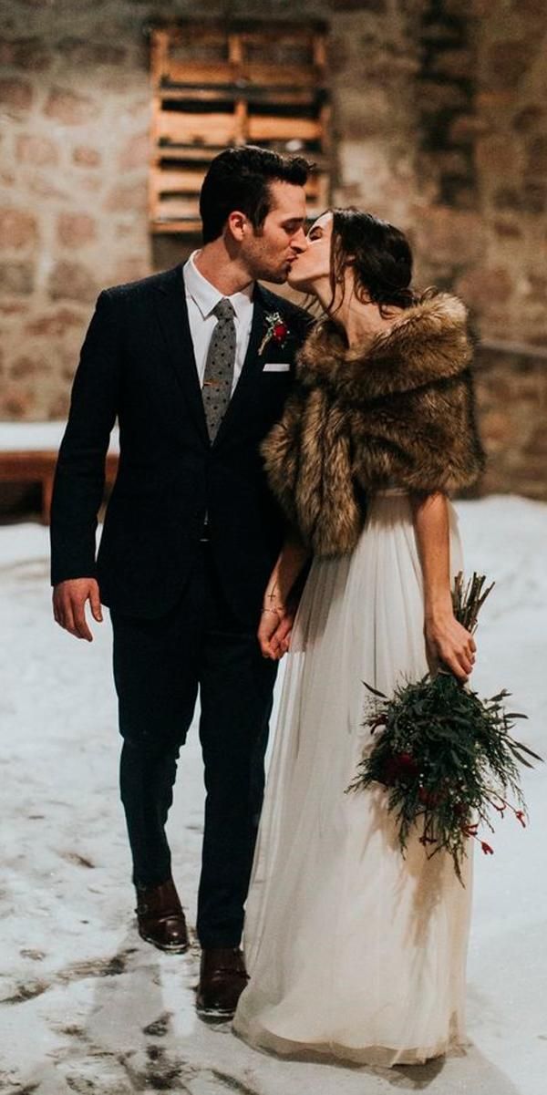 a bride and groom are kissing in the snow with their fur stole around their shoulders