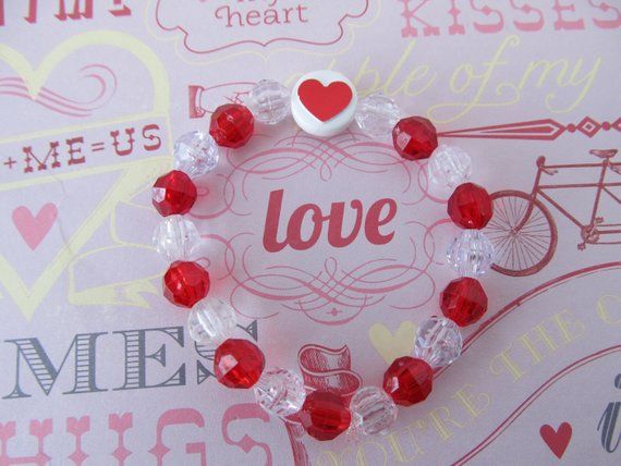 a heart shaped bracelet with red and white beads on top of a pink paper background