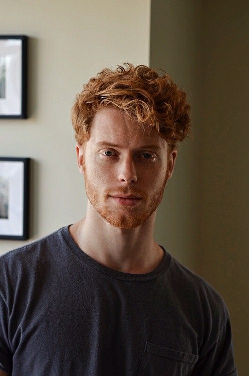 a man with red hair and beard standing in front of pictures