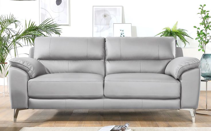 a grey leather couch sitting on top of a wooden floor next to a potted plant