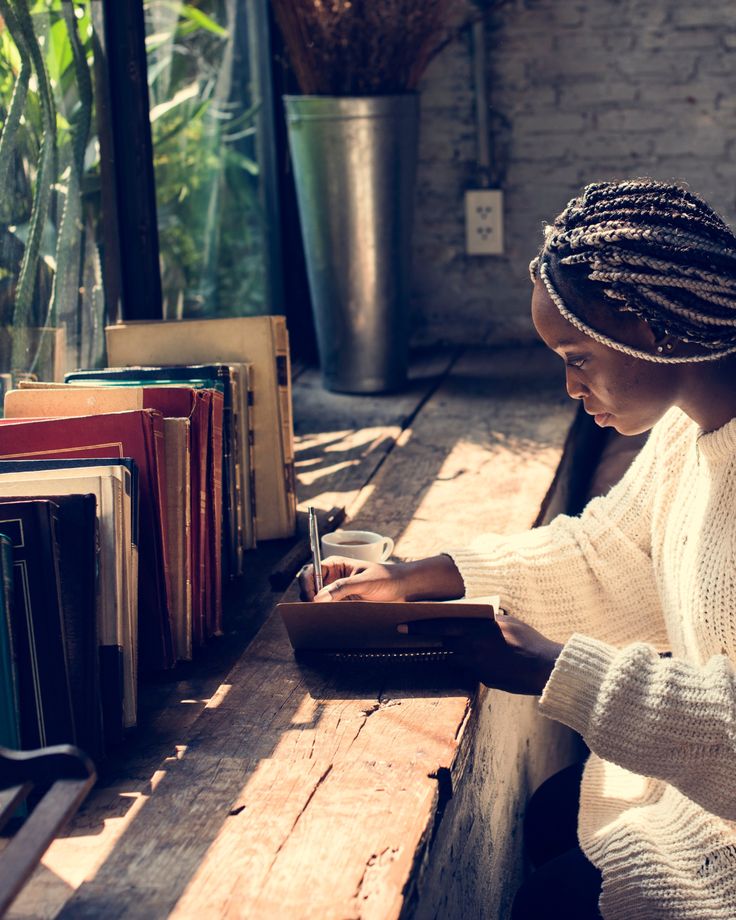 a woman is sitting at a table with books and writing on a book case while holding a pen