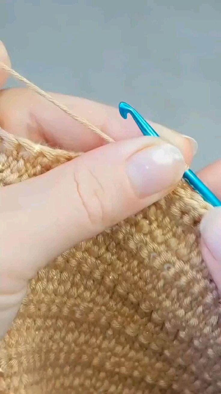 a woman is knitting with a blue crochet hook in her left hand and another person's right hand holding the yarn