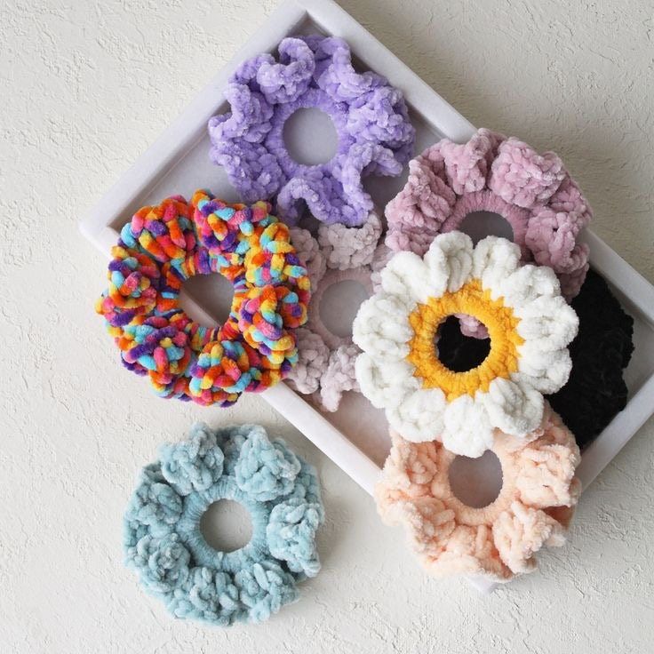 four crocheted scrunffles are arranged on a white tray and one is in the shape of a flower