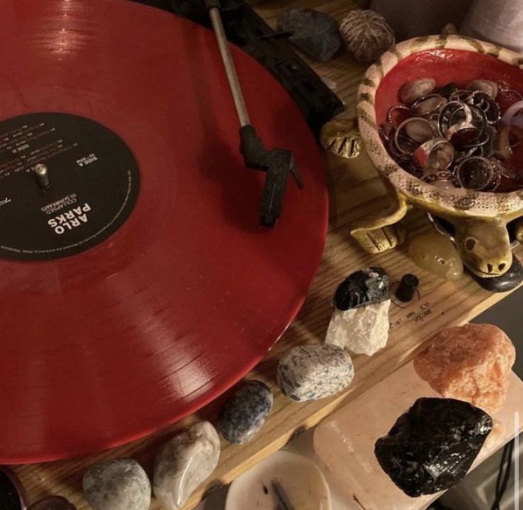 a red record player sitting on top of a wooden table next to other records and rocks