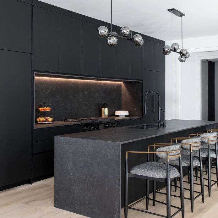 a kitchen with black cabinets and marble counter tops, along with bar stools in front of an island