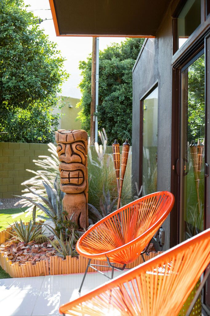 two orange chairs sitting on top of a patio next to plants and trees in front of a building