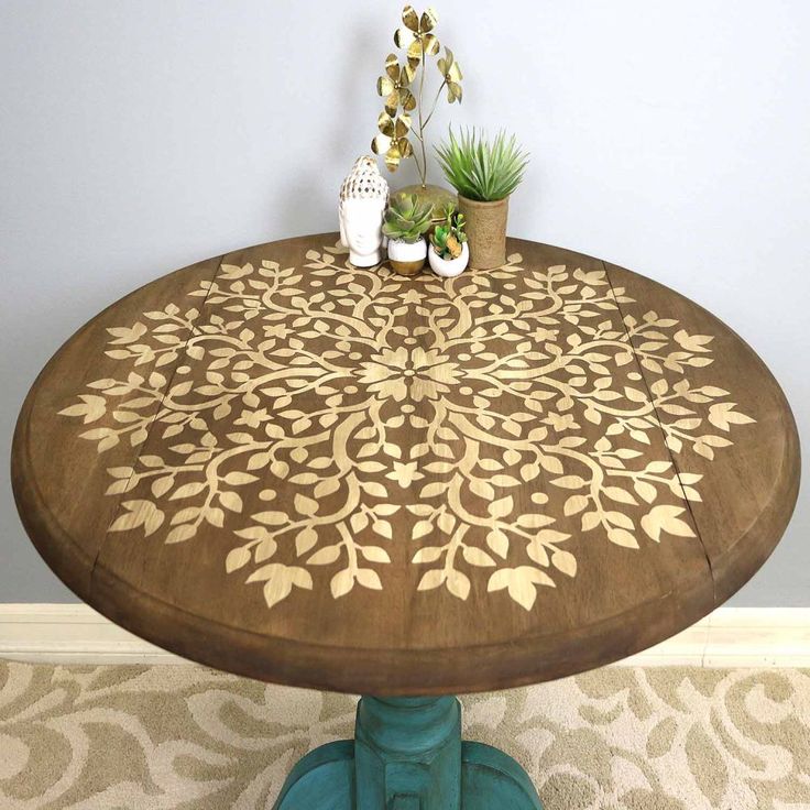 a wooden table with an intricate design painted on it and two potted succulents