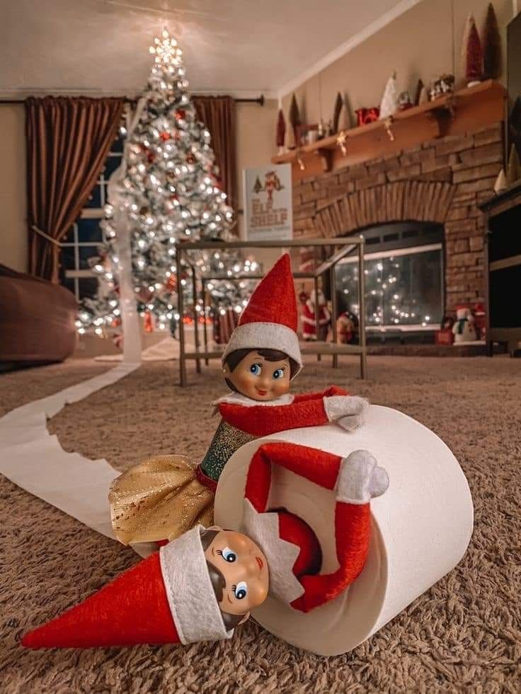 two elfs sitting on top of a roll of toilet paper in front of a christmas tree