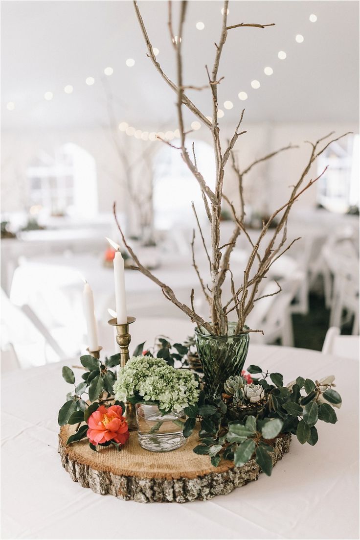 a centerpiece with candles, flowers and greenery sits on a table in a white room