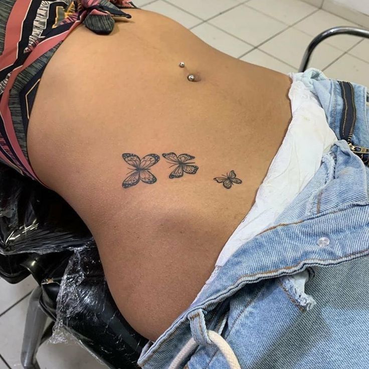 the back of a woman's stomach with three butterflies tattoo on her left side