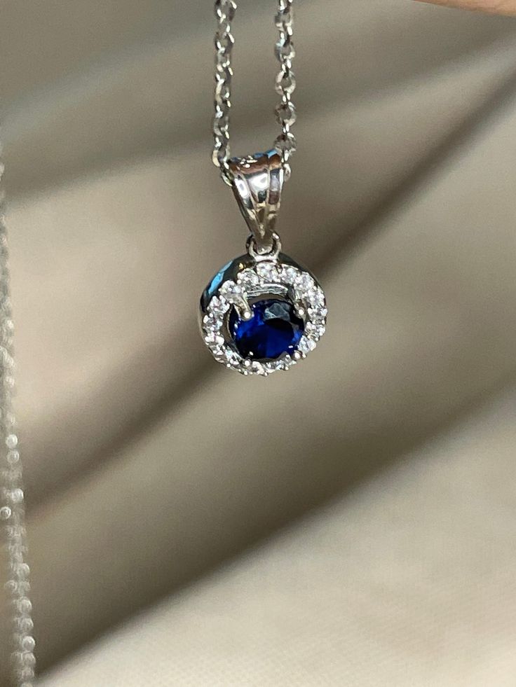 One Carat Round Cut Natural Blue Sapphire Necklace with halo diamonds necklace The depth and richness of the blue in this sapphire is reminiscent of velvet. Safely ensconced in a dazzling halo of pave diamonds (.50 carats-worth), this one-carat blue sapphire is absolutely dripping in elegance. This stunning necklace easily goes from the office to a romantic night in the town without missing a beat. In addition to ensuring a fabulous September birthday, this piece also doubles as a delightful 45t Luxury Round Sapphire Diamond Necklace, Formal Blue Diamond Necklace, Formal Sapphire Diamond Necklace With Brilliant Cut, Formal Sapphire Pendant Diamond Necklace, Formal Blue Diamond Gemstone Necklace, Formal Blue Gemstone Diamond Necklace, Formal Round Sapphire Necklaces, Sapphire Necklace With Prong Setting, Classic Round Sapphire Diamond Necklace