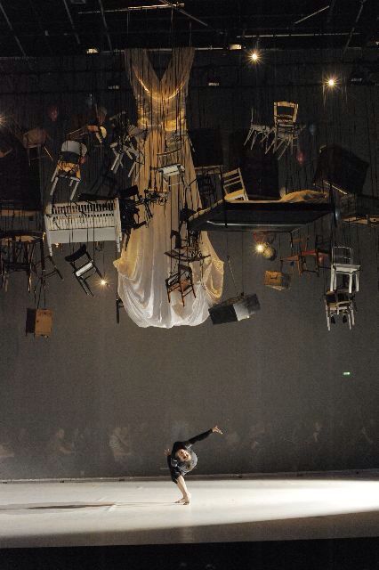 a person standing on a stage with chairs hanging from the ceiling