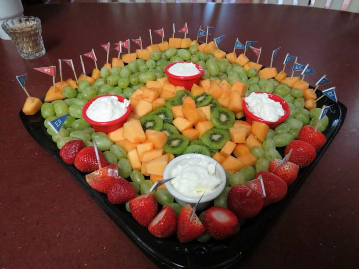 a platter filled with fruit and dips on top of a wooden table next to a glass of water