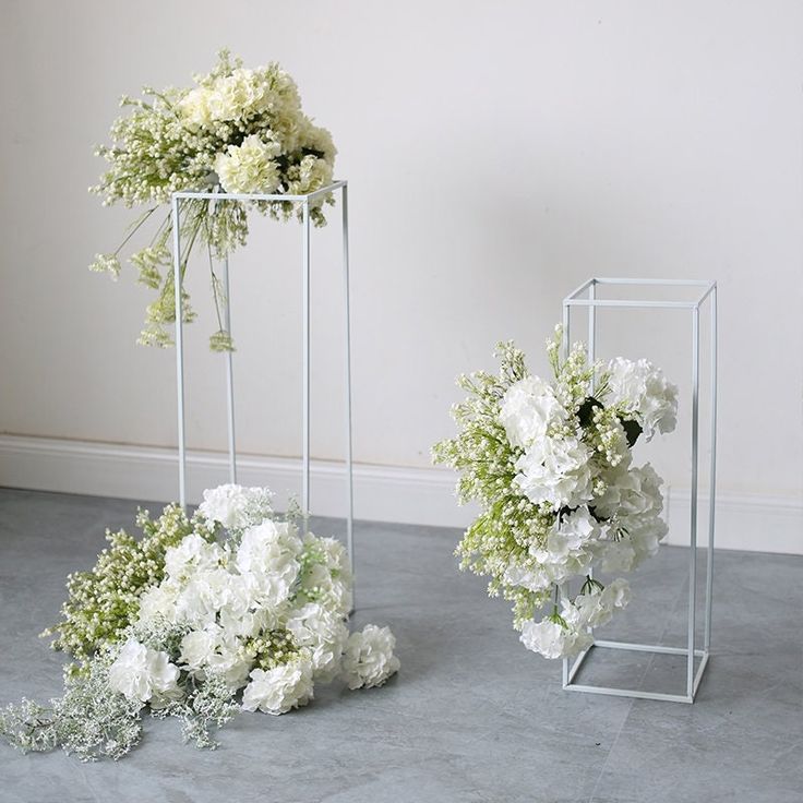 two vases filled with white flowers sitting on top of a floor next to each other