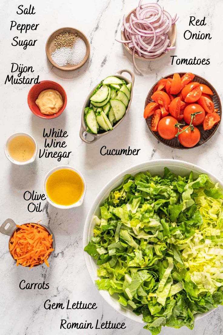 the ingredients for a salad laid out on a marble counter top, including carrots, cucumbers, onions, red onion and lettuce