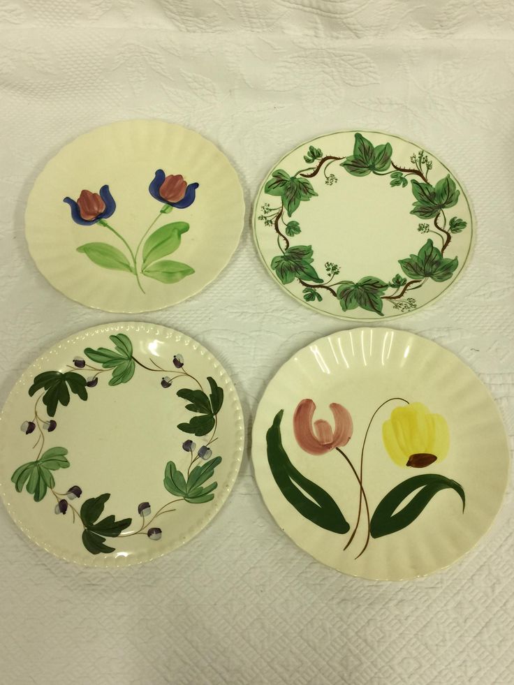 four plates with flowers painted on them sitting on a white tablecloth covered table cloth