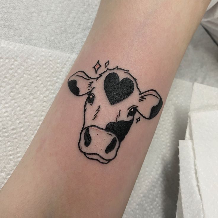 a black and white cow with a heart on it's face is shown in this tattoo