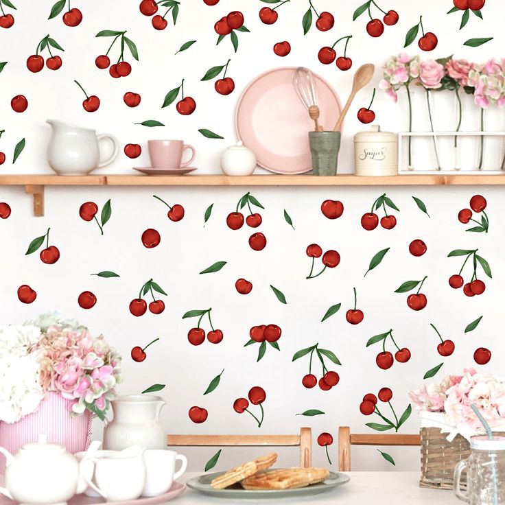 a wall with cherries on it next to plates and cups in front of a shelf