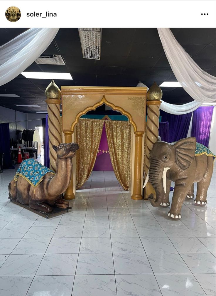 two statues of elephants and a camel in front of a stage with drapes on it