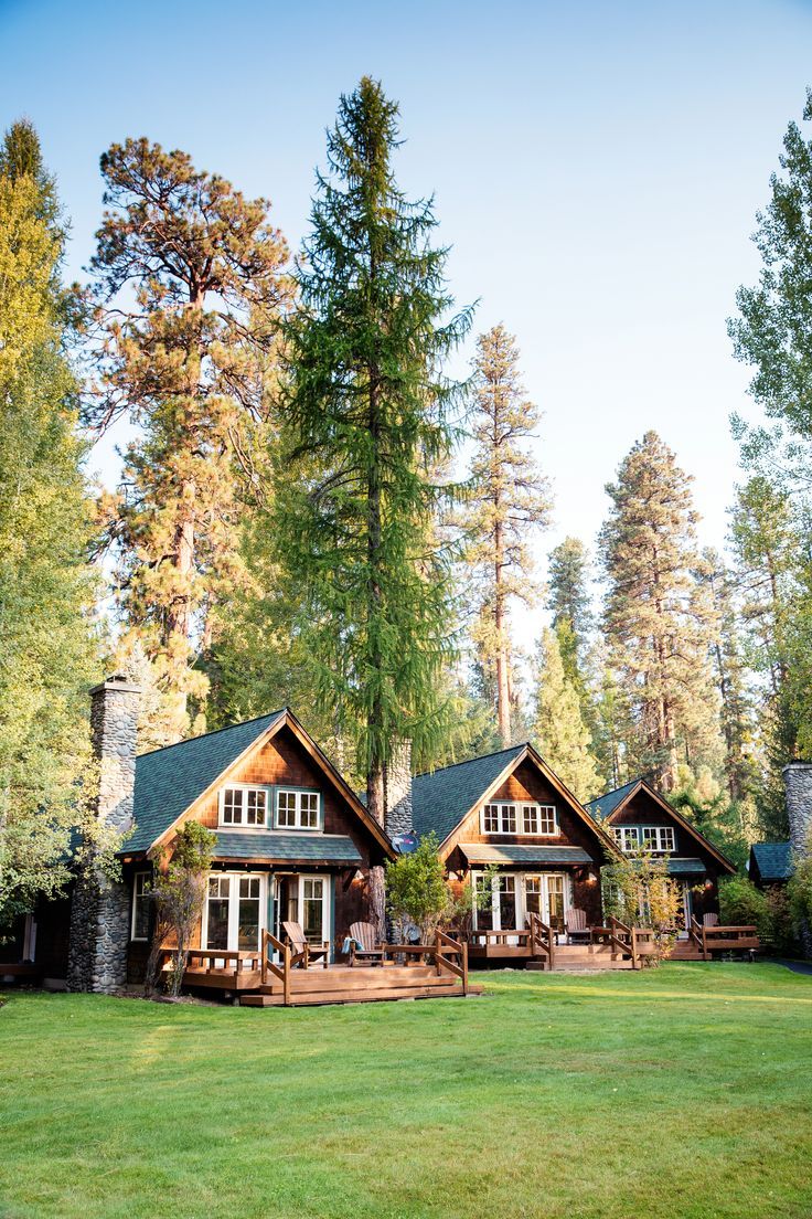 a house in the woods with lots of trees and grass on the front lawn, surrounded by tall pine trees