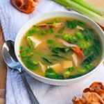 a white bowl filled with soup next to green onions and celery on top of a table