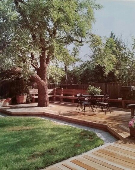 a wooden deck surrounded by green grass and trees in the back yard with seating area