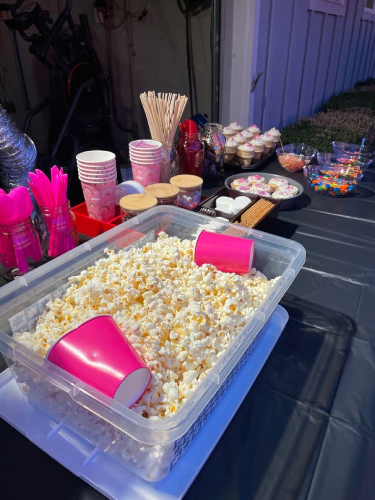 a plastic container filled with popcorn sitting on top of a table next to other food