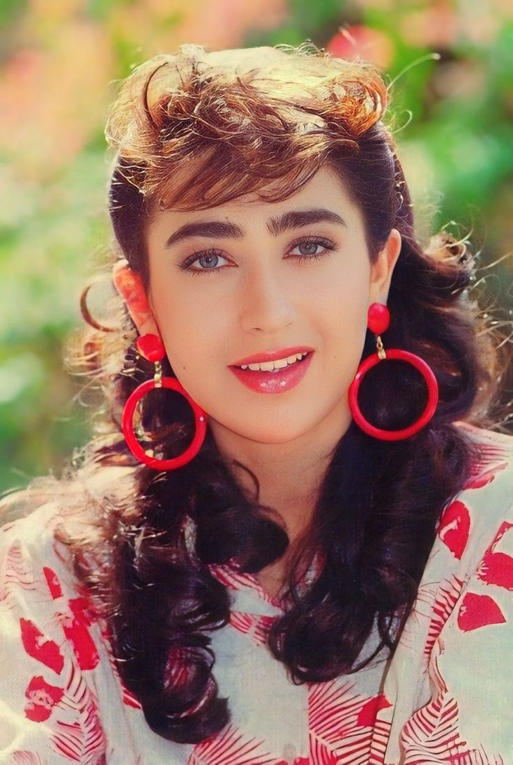 a close up of a person wearing large red hoop earrings and a white shirt with trees in the background