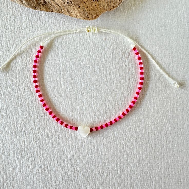 a red and white beaded bracelet with a heart charm on it next to a rock