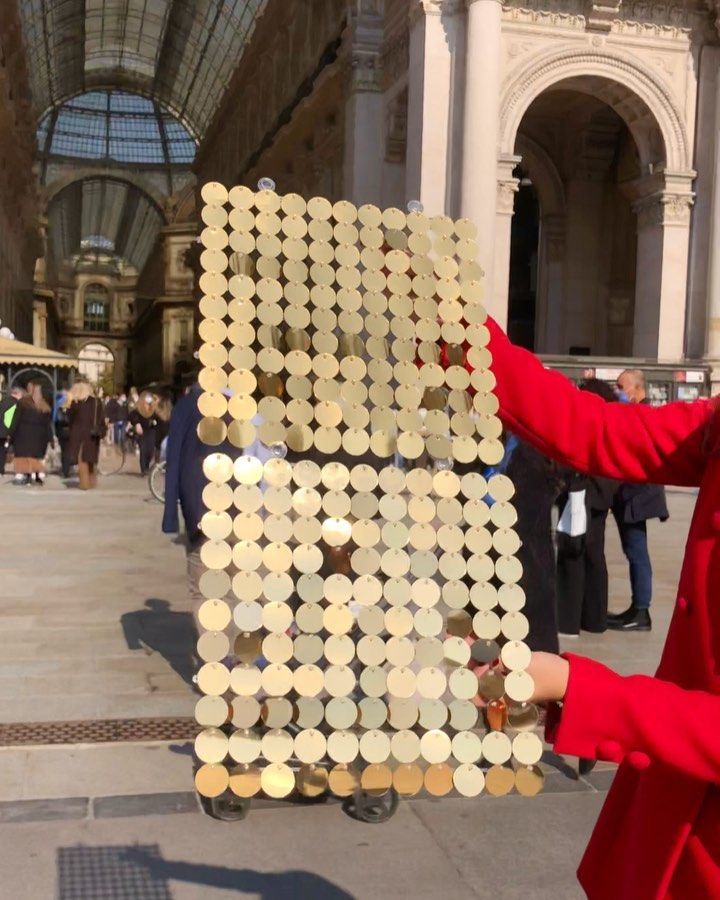 a woman in a red coat is holding up a sign made out of circles on the sidewalk