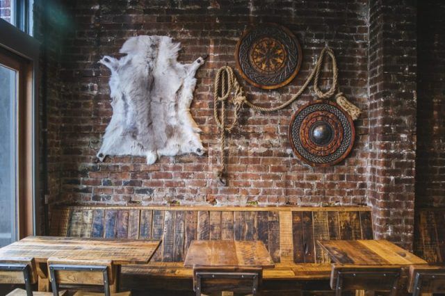 a brick wall with several wooden tables and chairs in front of it, along with an animal skin rug hanging on the wall