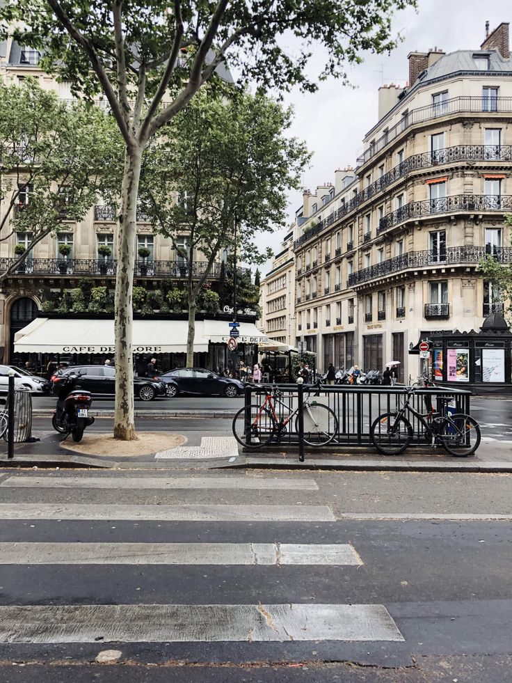 an empty street with cars parked on the side and people sitting at tables in the middle