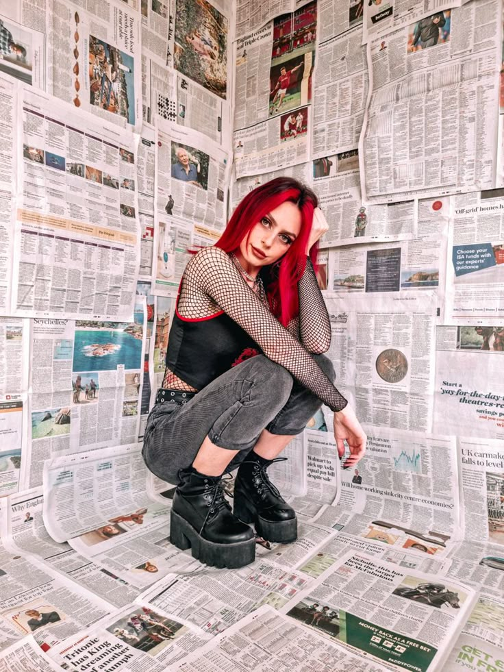 a woman sitting on top of a pile of newspaper next to a wall covered in newspapers