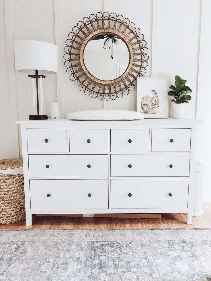 a white dresser with lots of drawers and a round mirror above it