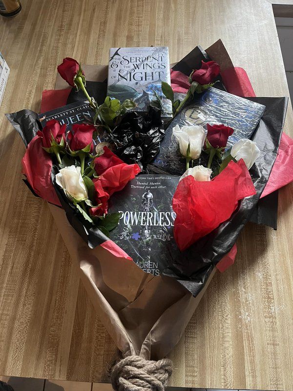 a bouquet of roses wrapped in paper on top of a wooden table next to a book