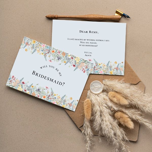 two wedding cards on top of an envelope with feathers and a pen next to it