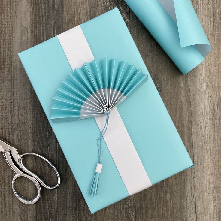 a gift wrapped in blue and white paper with a hand fan on it next to scissors