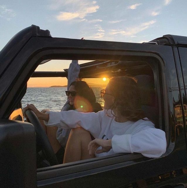 two people are sitting in the back of a truck looking out at the ocean while the sun is setting