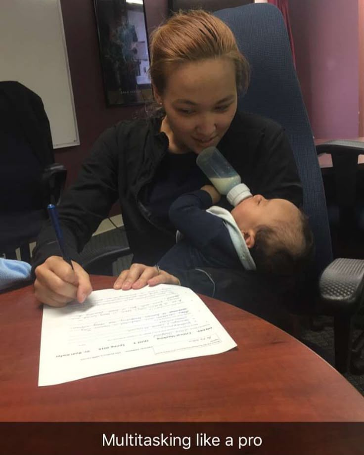 a woman sitting at a desk with a baby in her lap and writing on a piece of paper